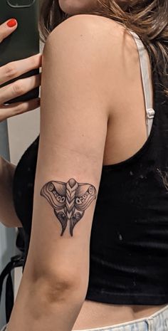 a woman with a moth tattoo on her arm holding a cell phone and taking a selfie