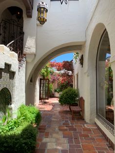 an arched walkway with benches and potted plants on either side, between two buildings