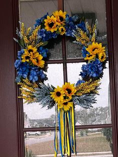 a wreath with sunflowers and blue flowers hanging from the side of a window