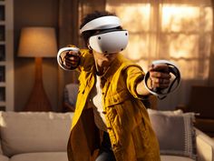 a man wearing a yellow jacket and white helmet playing with a wii mote in his living room