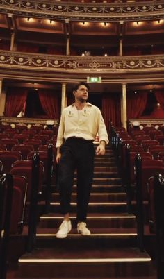 a man standing at the bottom of some stairs in front of an auditorium with red curtains