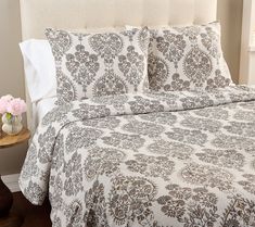 a bed with a white and brown bedspread on top of it next to a night stand