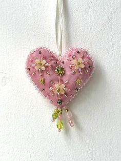 a pink heart shaped ornament hanging from a white wall with flowers on it