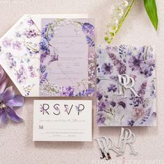 the wedding stationery is laid out on the floor with purple flowers and greenery