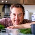 a man is smiling while leaning on a counter in the kitchen next to some vegetables