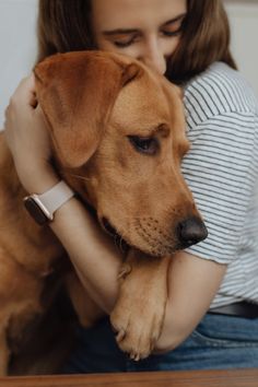 a woman is hugging her dog while sitting on the floor with it's eyes closed