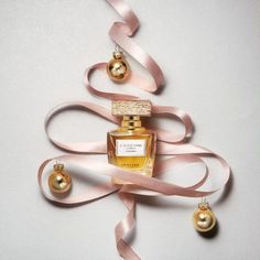 a bottle of perfume sitting on top of a pink ribbon next to christmas balls and ornaments