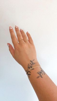 a woman's hand with tattoos on her left wrist and gold chain around the wrist