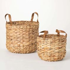 two woven baskets sitting next to each other on a white surface with brown leather handles