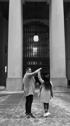 a man and woman standing in front of a building pointing at something with their hands