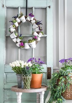 two potted plants are sitting on a table next to an old door with a wreath