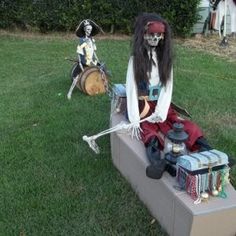 two skeletons sitting on top of a cement block in the grass next to a statue