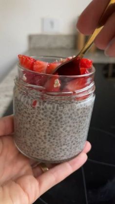 a person holding a spoon in a jar filled with chia seeds and strawberries