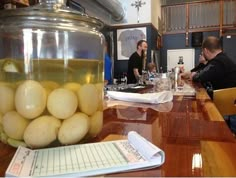 two men sitting at a table with some food in a jar on top of it