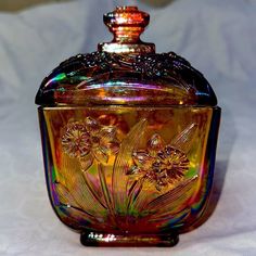 a glass jar with flowers painted on the side and lid sitting on a white surface