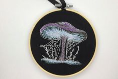 a black and yellow embroidered wall hanging with a purple mushroom on it's side