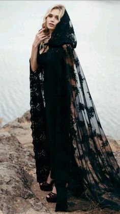 a woman standing on top of a rock next to the ocean wearing a black dress