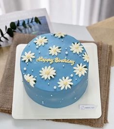 a blue birthday cake with white daisies on it sitting on top of a plate