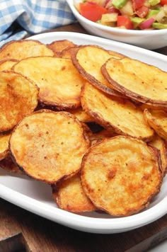 some potato chips on a white plate next to a bowl of salad and a wooden cutting board