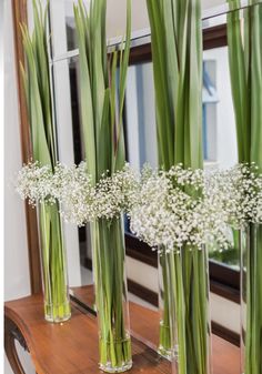 three vases filled with white flowers on top of a wooden table next to a mirror