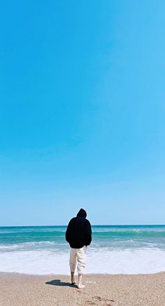 a man standing on top of a sandy beach next to the ocean under a blue sky