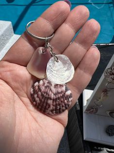 a person is holding a sea shell keychain in their left hand while wearing a ring