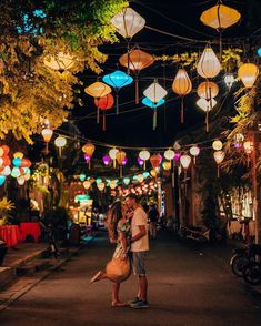 a man and woman standing in the middle of an alley at night with lanterns hanging above them