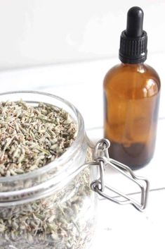 a glass jar filled with herbs next to a bottle of liquid