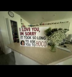 a sign sitting on top of a kitchen counter next to a vase with flowers in it