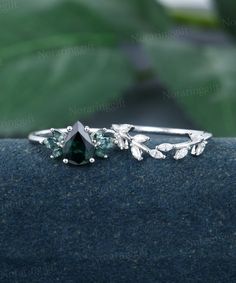 a close up view of a ring with leaves on the side and a green stone in the middle