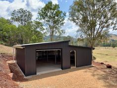 a large metal building sitting in the middle of a field next to trees and dirt