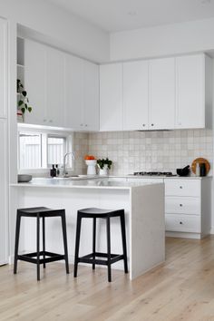 two stools sit in front of an island countertop with white cabinets and drawers