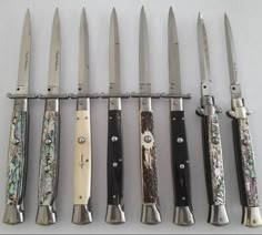 six knives are lined up in a row on a white surface with floral designs and silver handles