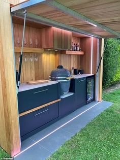 an outdoor kitchen with cabinets and wine glasses on the counter top, under a wooden roof