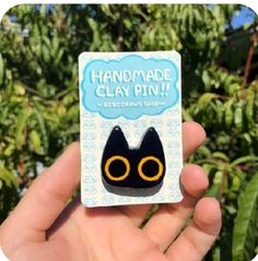 a handmade clay pin with an image of a black cat's eyes and the words handmade clay on it