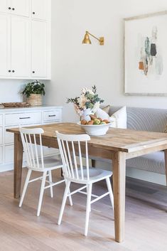 a dining room table with white chairs and a bowl of fruit on it