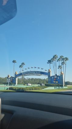 the entrance to an amusement park with palm trees in the foreground and blue sky above