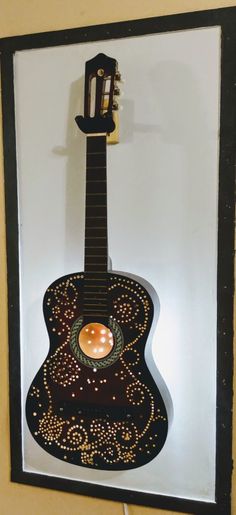 an acoustic guitar is hanging on the wall in front of a white background and black frame