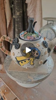 a teapot with a cat on it sitting on top of a table