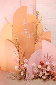 an arrangement of flowers is displayed in front of a pink backdrop with arches and round shapes