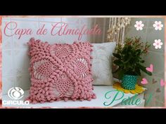 a pink crochet pillow sitting on top of a white table next to a potted plant