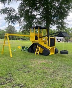 a yellow playground set in the middle of a grassy field next to a large tree