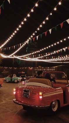 an old red car parked in front of a building with lights on the ceiling and decorations hanging above it