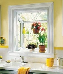 a kitchen with yellow walls and white counter tops has flowers in the window sill