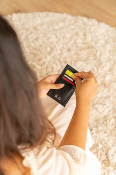 a woman is sitting on the floor and playing with her credit card wallet while holding it in one hand