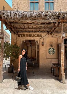 a woman standing in front of a starbucks building with her hand on her hip bag