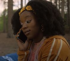 a woman sitting in the woods talking on her cell phone while wearing a flower headband