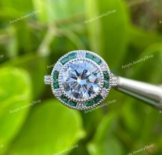 a diamond ring with green and white stones on it sitting on top of a plant