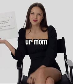 a woman sitting in a chair holding up a sign with the words ur mom on it