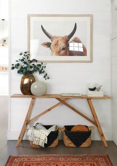 a cow is on the wall above a wooden table with baskets and plants in front of it